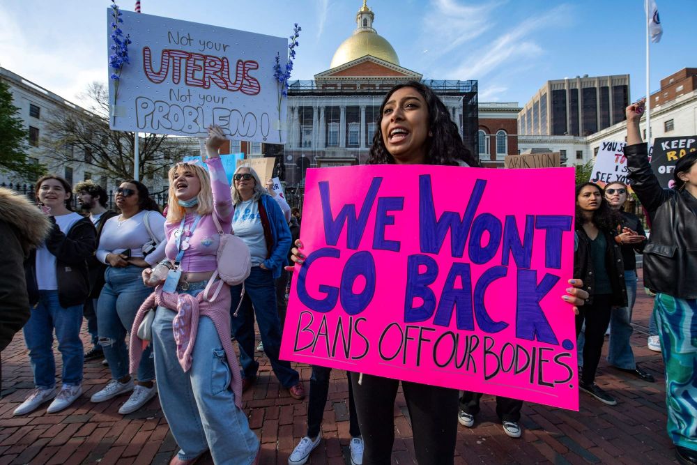 pro-choice demonstrators stand outside of the Boston State House. a person in the foreground holds a large pink poster that r