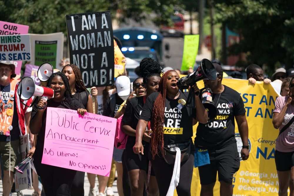 color photograph of pro-choice protesters walking in the streets. most wear all black and hold signs with slogans like "publi