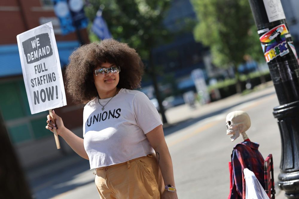 color photograph of a black woman with natural hair at an outdoor protest. she wears a white t-shirt that says "union" in bla