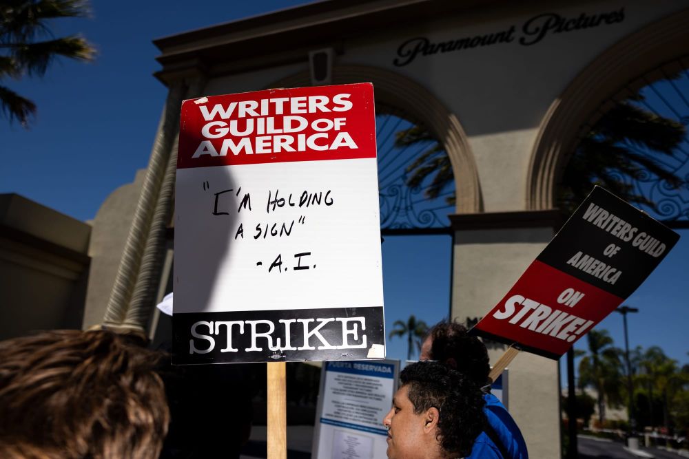 color photograph of an outdoor protest in support of the Writers Guild of America. a picket sign is slightly off center in th