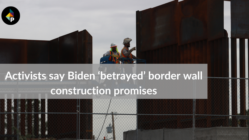 color photograph of two workers in orange safety vests and hard hats on a construction lift. they examine a section of the bo