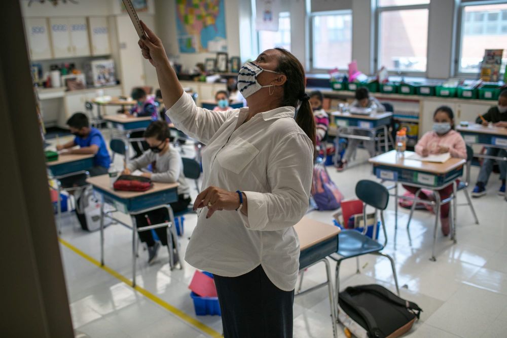 color photograph of a female teacher wearing a face mask and white button-down shirt. she stands in the center of the frame a