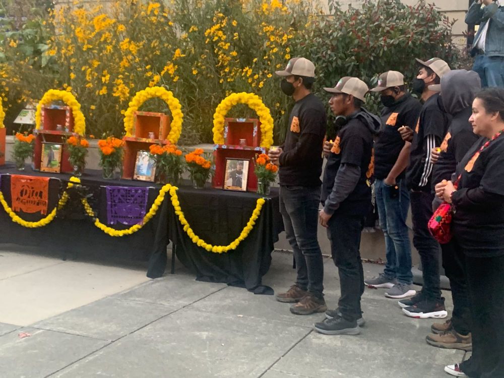 color photograph of about five farmworkers and farmworker advocates wearing dark clothing and face masks standing to the righ