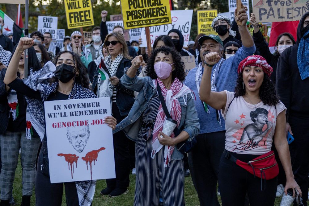 outdoor protest of pro-Palestine protestors marching with sign that reads "In November we'll remember Genocide Joe"
