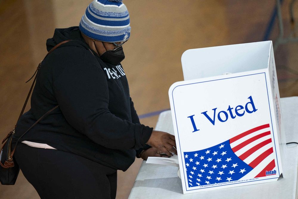 color photograph of a Black woman wearing a blue striped beanie and a face mask at a voting booth