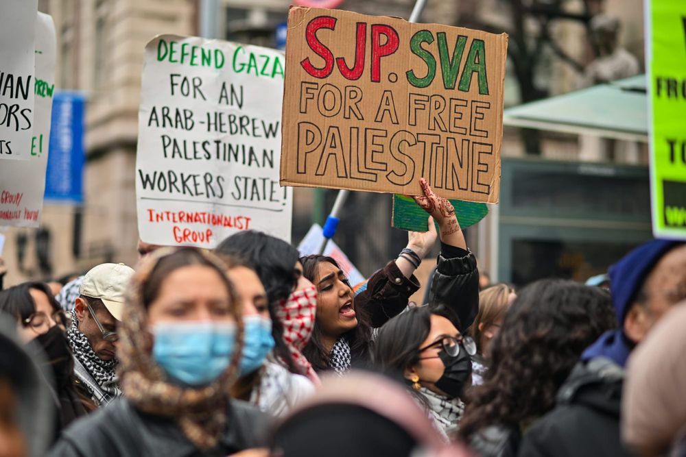 color photograph of an outdoor protest in support of Palestinian liberation. people wear face masks as they hold signs readin