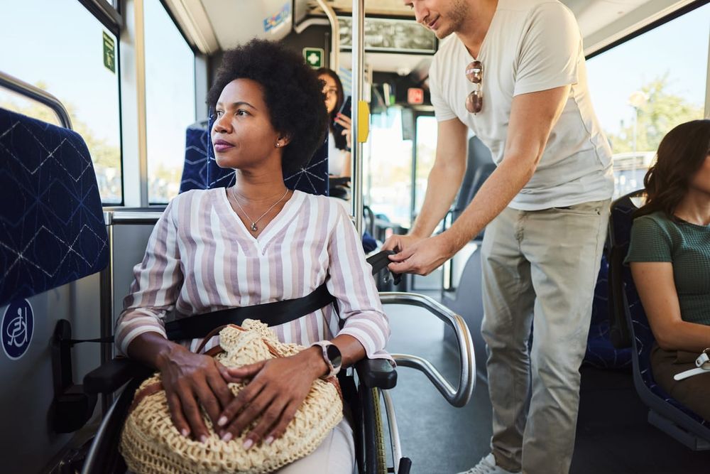 color stock photo of a Black woman wearing a striped long-sleeve shirt. she sits in a wheelchair on a public transit bus