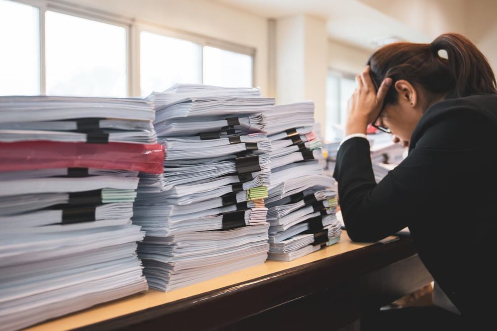 color photograph of a stressed lawyer sitting at a desk with several piles of paperwork beside her