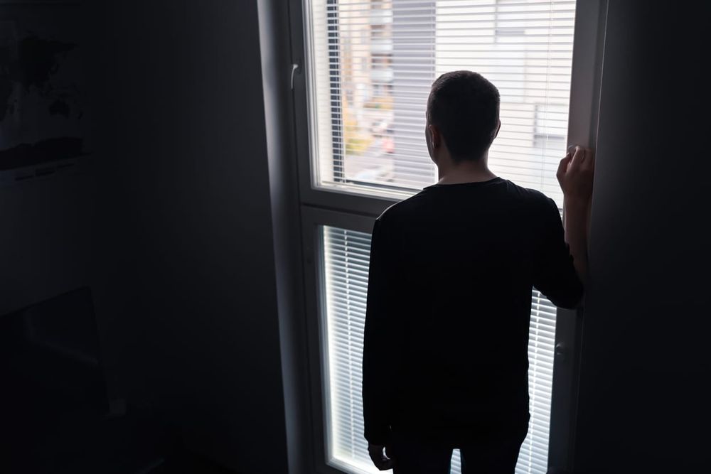 dark photograph of a young man looking out a window