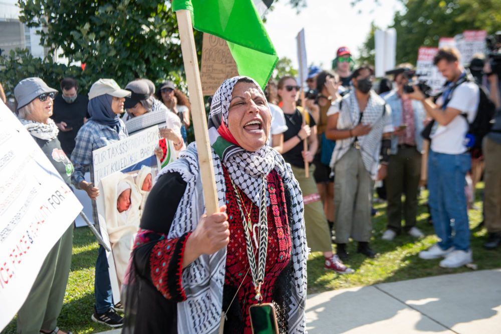 color photograph of a woman wearing a keffiyeh yelling as she holds a picket sign just out of frame