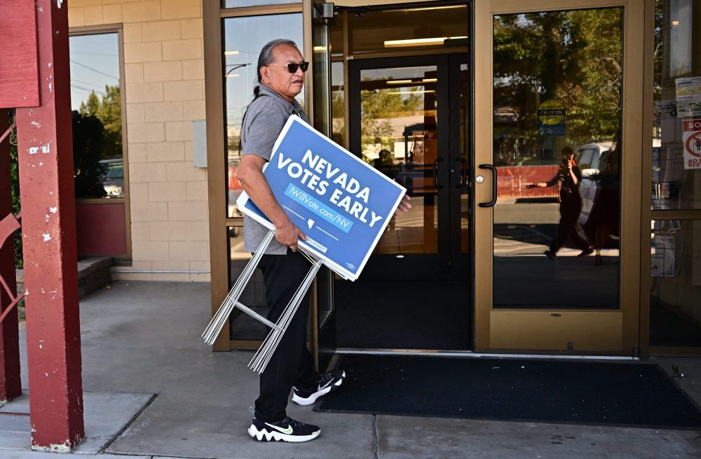 A man holds a sign reading "Nevado votes early" outside of a pair of glass doors.
