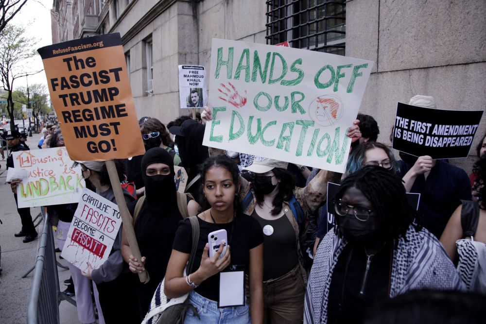 protesters hold signs that read "Hands off our education" and "The fascist Trump regime must go!"