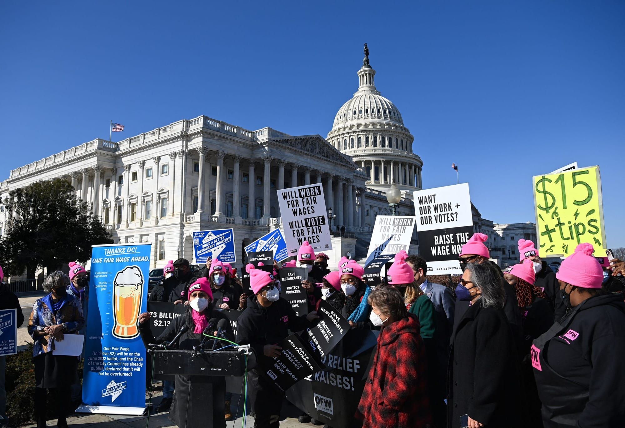 a dense crowd stands outside the U.S. Capitol holding signs in support for $15 minimum wage and better workers' rights