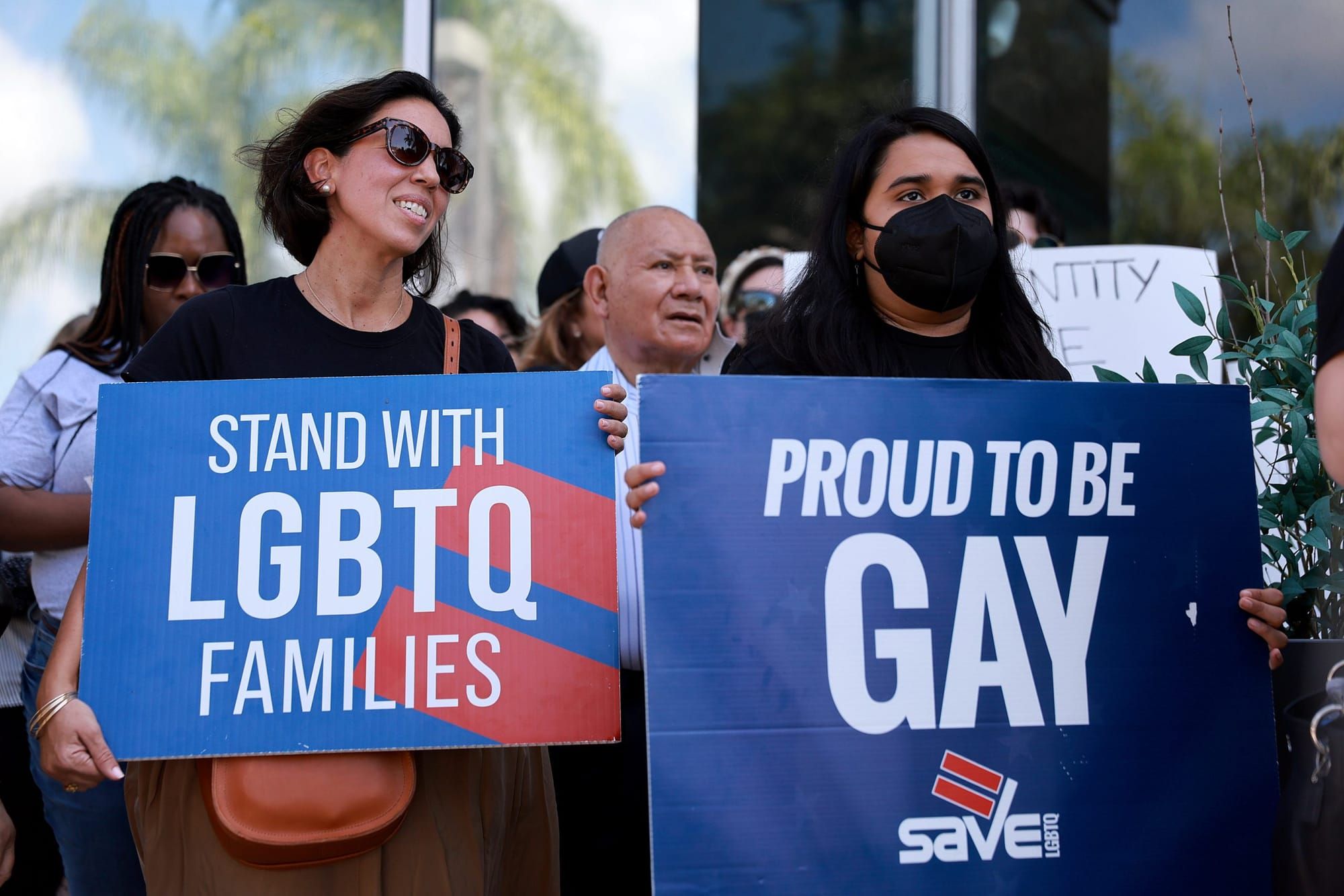 people hold signs reading "Stand with LGBTQ families" and "Proud to be gay"