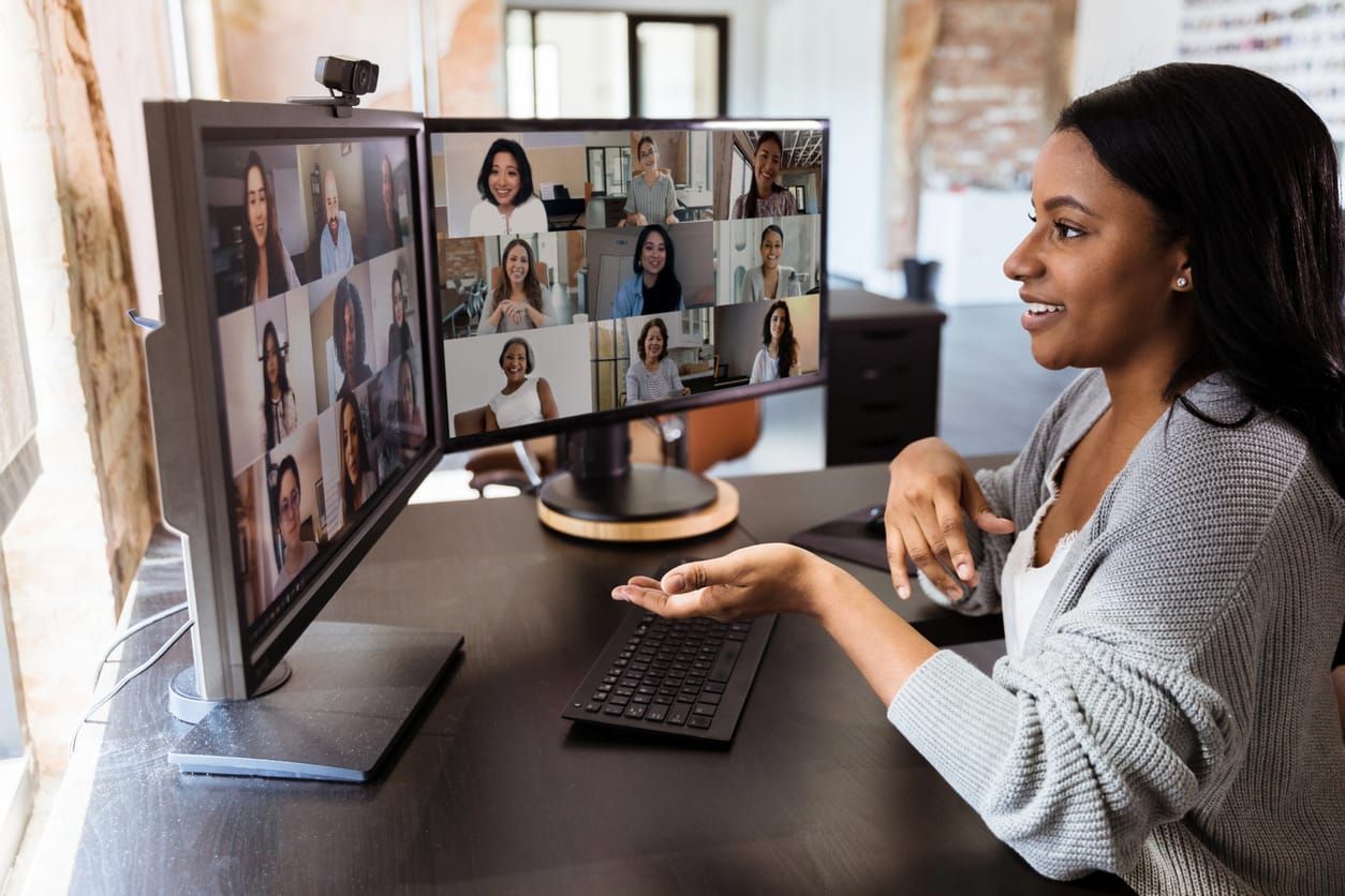 woman with dark brown skin and straight hair past her shoulders gestures on camera during a remote work virtual meeting