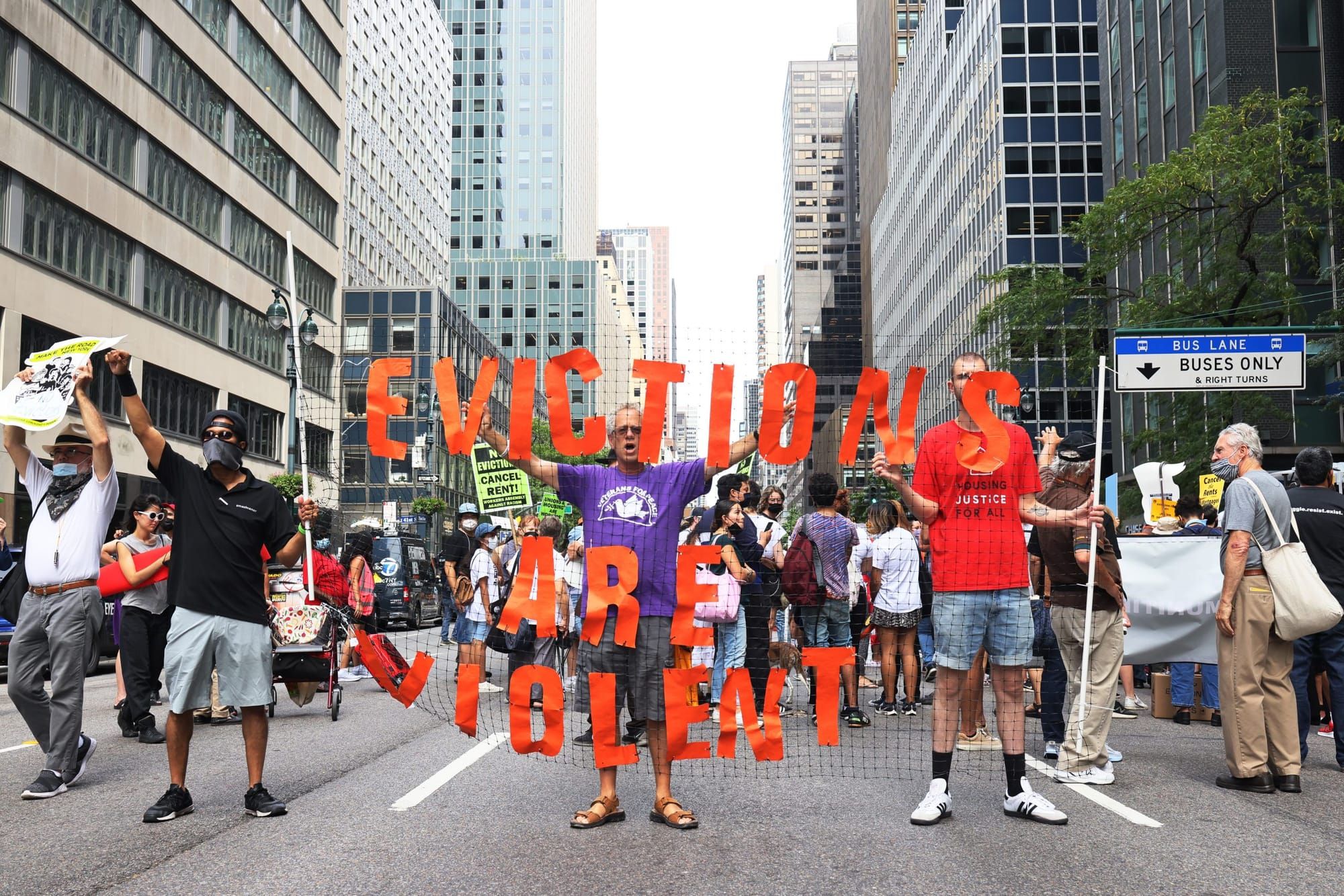 three people hold up a sign reading "eviction is violence" during a protest on a city street