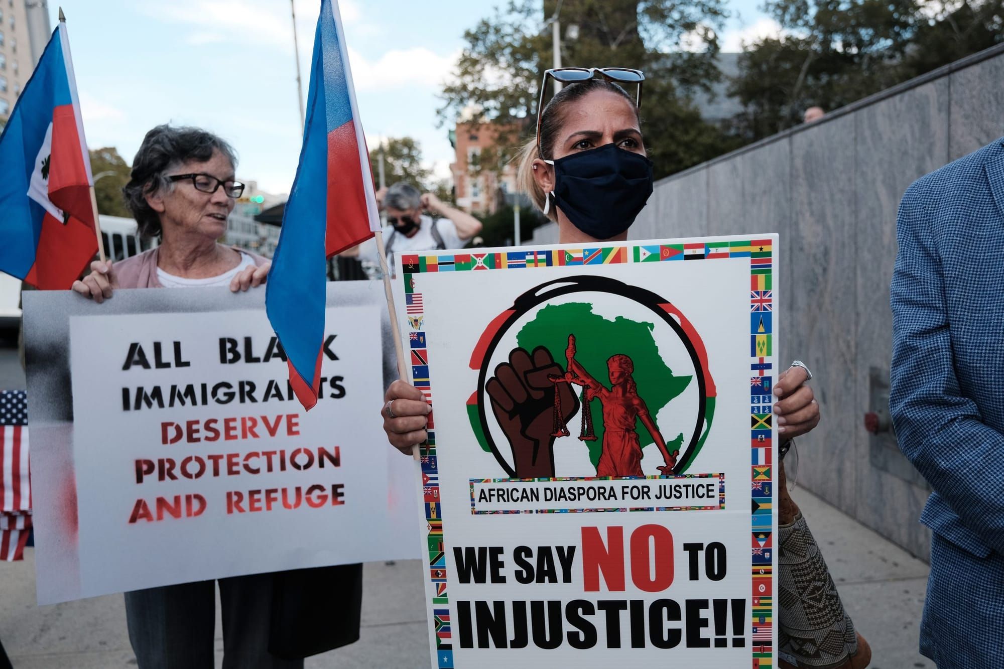 two women hold signs saying "we say NO to injustice!!" and "all Black immigrants deserve protection and refuge"