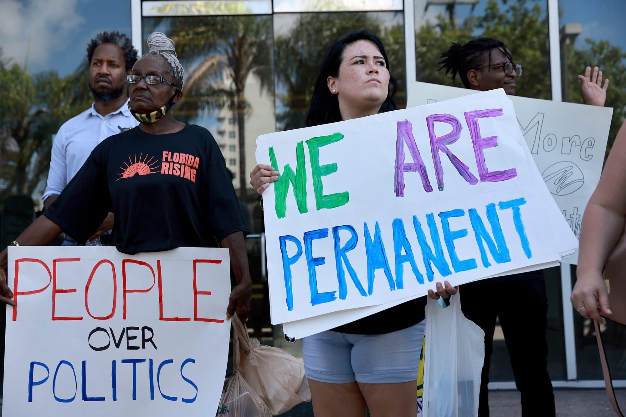 two people hold signs reading "we are permanent" and "people over politics"