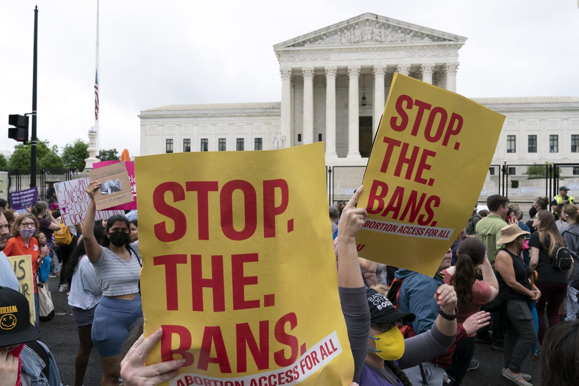 pro-choice protestors hold yellow signs with red text reading "stop the bans"