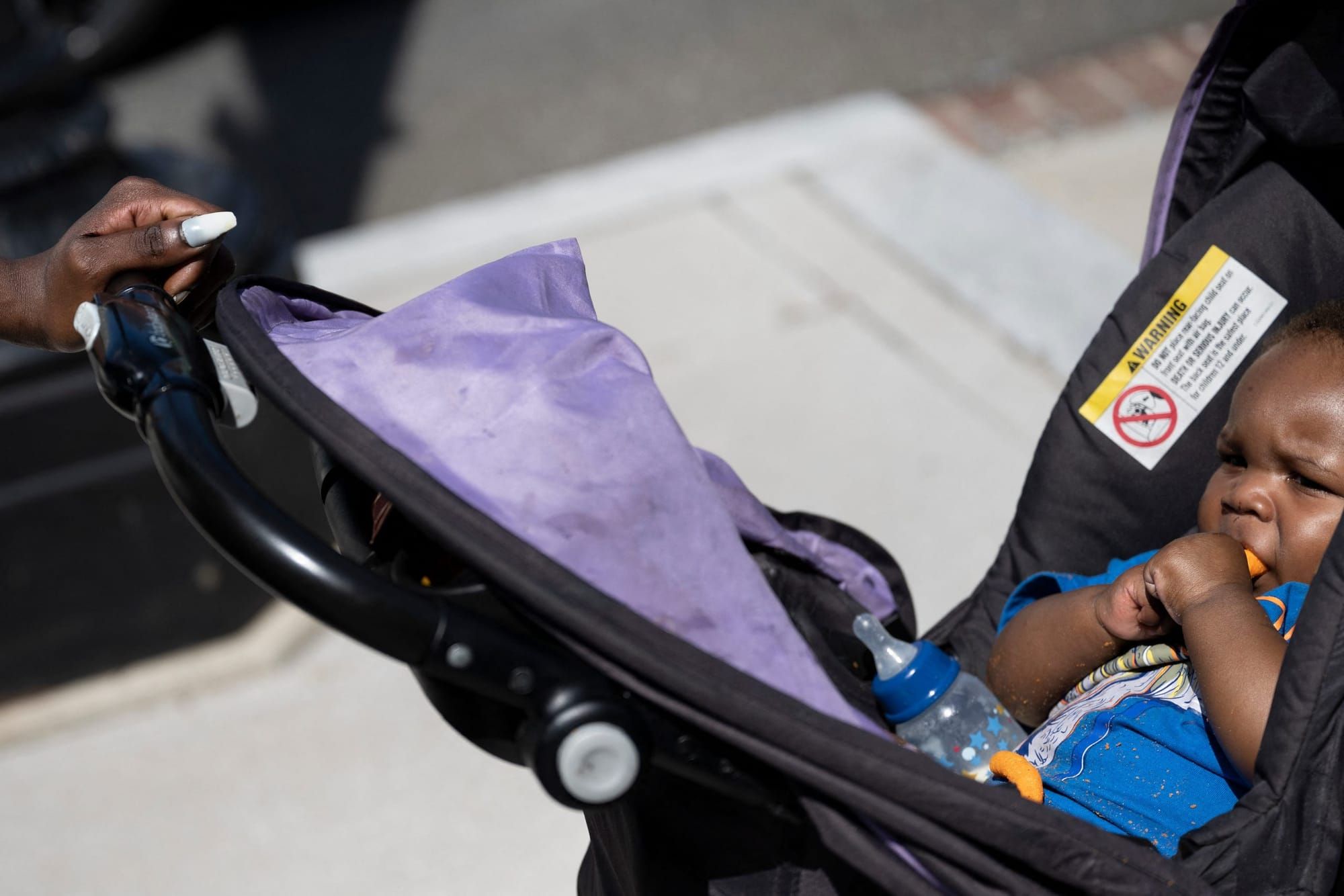 a Black baby rests in a stroller with a formula bottle in his lap