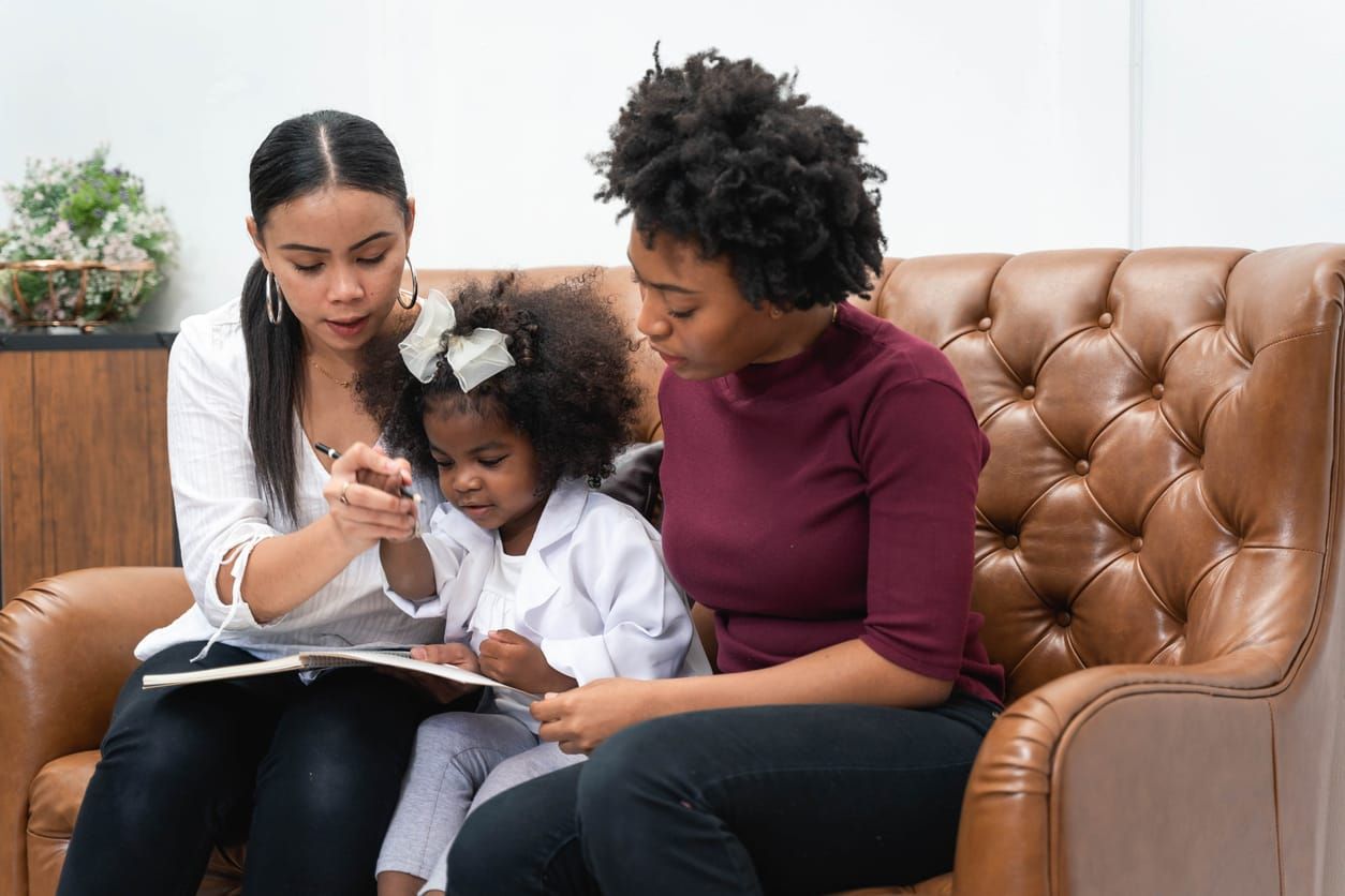 two Black mothers sit with their daughter