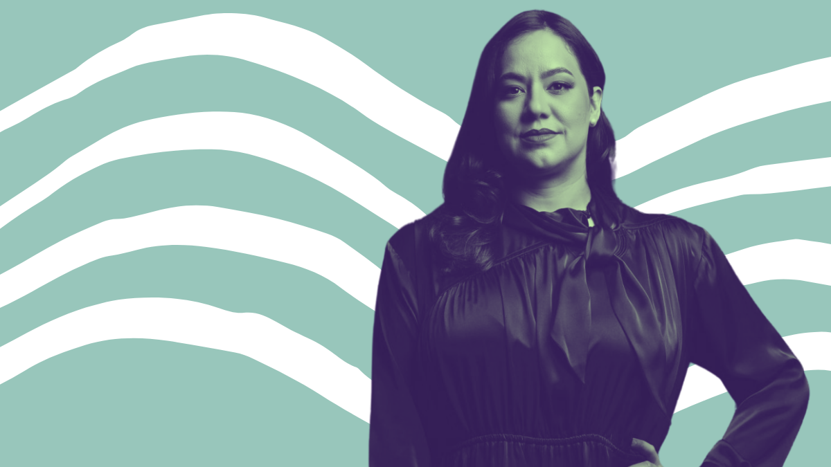 Rochelle Garza, a Latina with dark hair a few inches past her shoulders, wears a dark silky blouse in front of a turquoise an