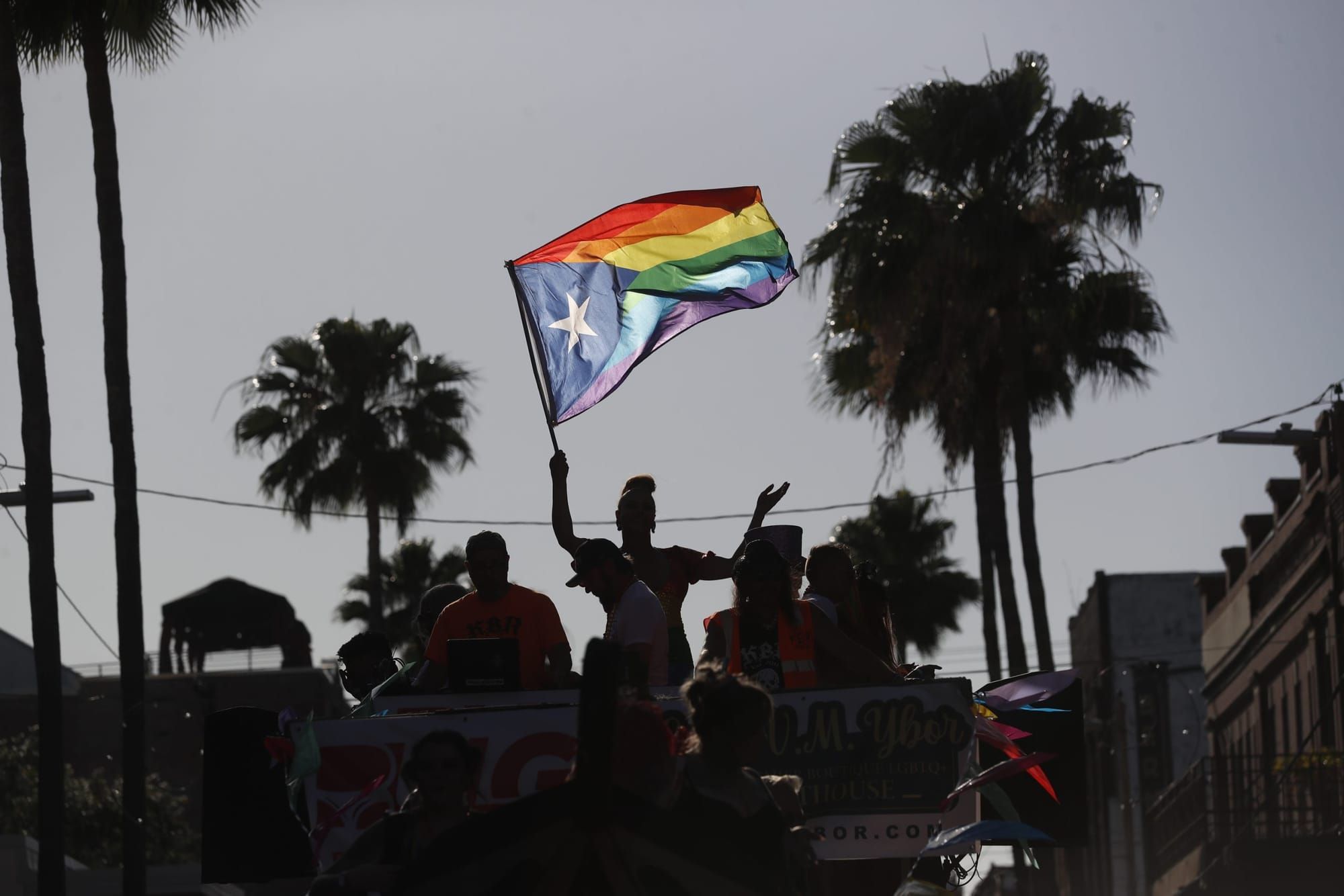 people stand on a Pride float and one person holds up a Pride and Puerto Rican flag