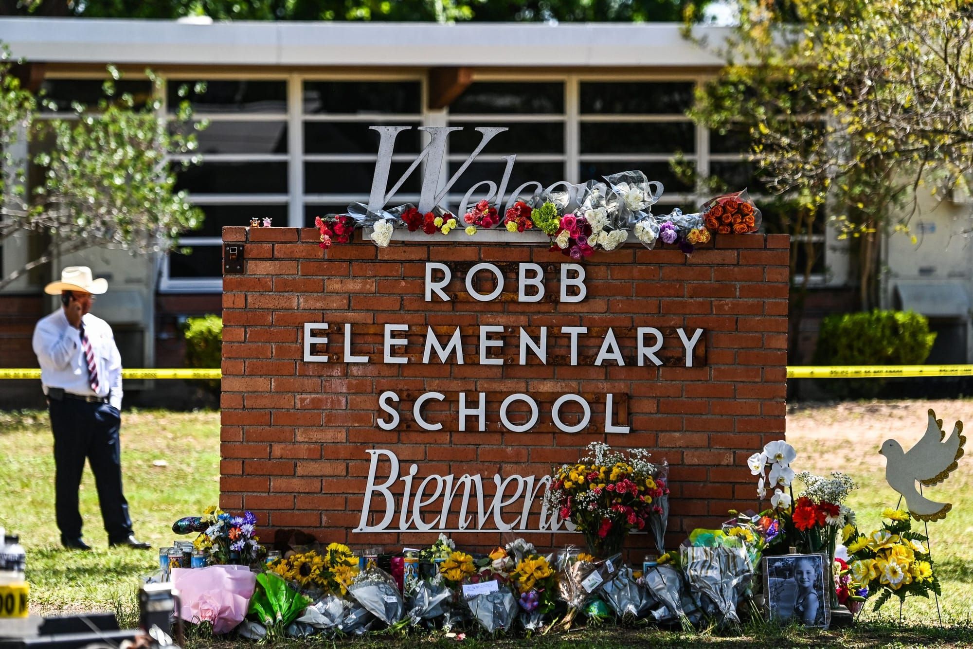 a brick sign with text reading "Robb Elementary School" with multiple bouquets of flowers left for the victims of the school