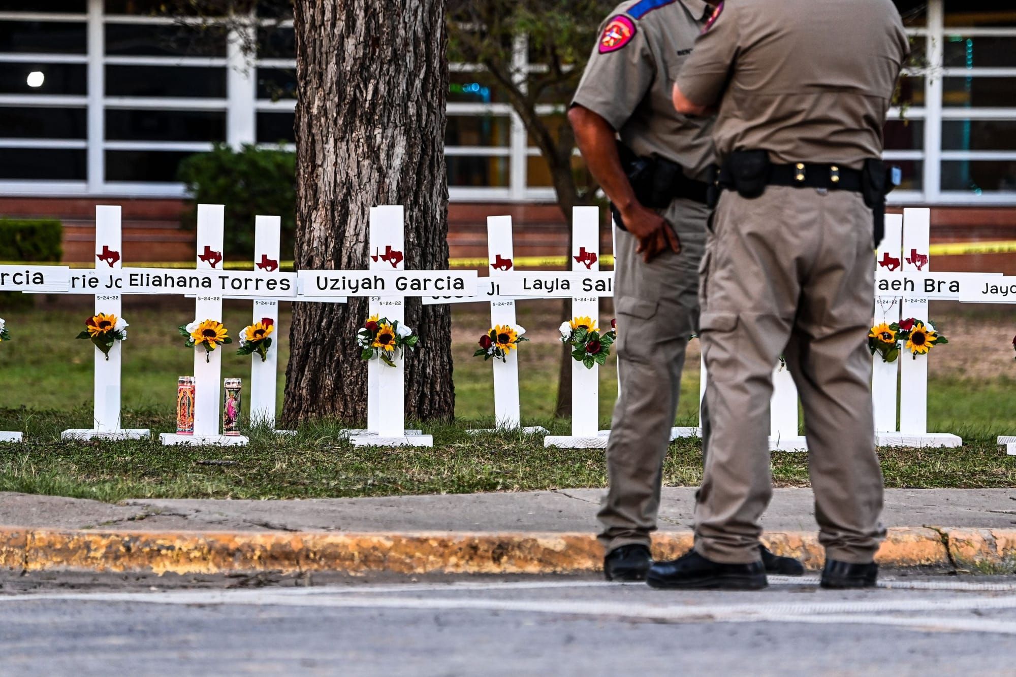 two law enforcement officers stand in front of a memorial for the students and teachers killed at the Robb Elementary School