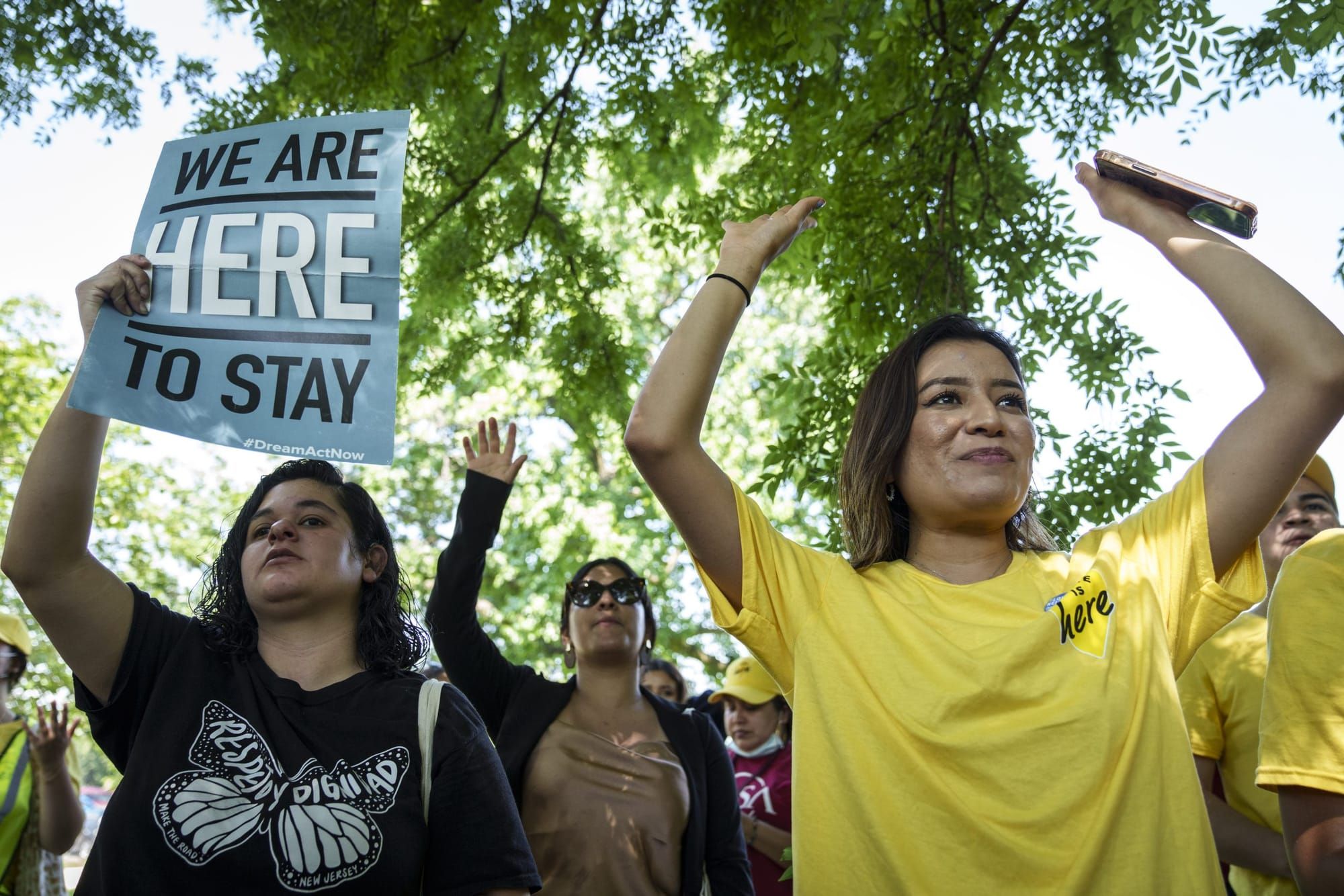 young immigrants and advocates hold signs saying "We are here to stay" in support of DACA