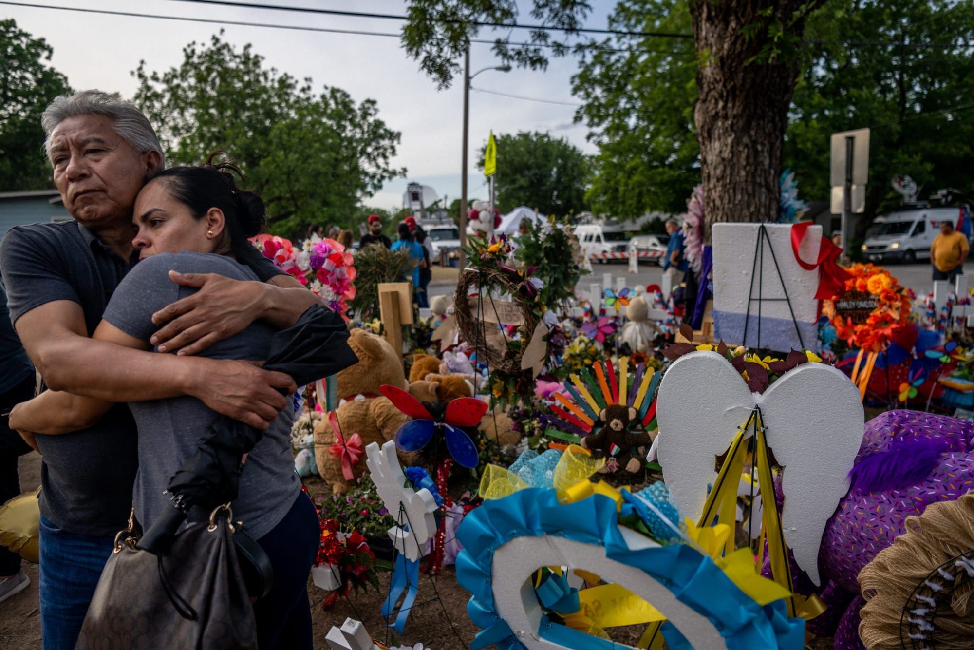 an older couple embraces in front of a memorial for the victims of the shooting at Robb Elementary in Uvalde, Texas
