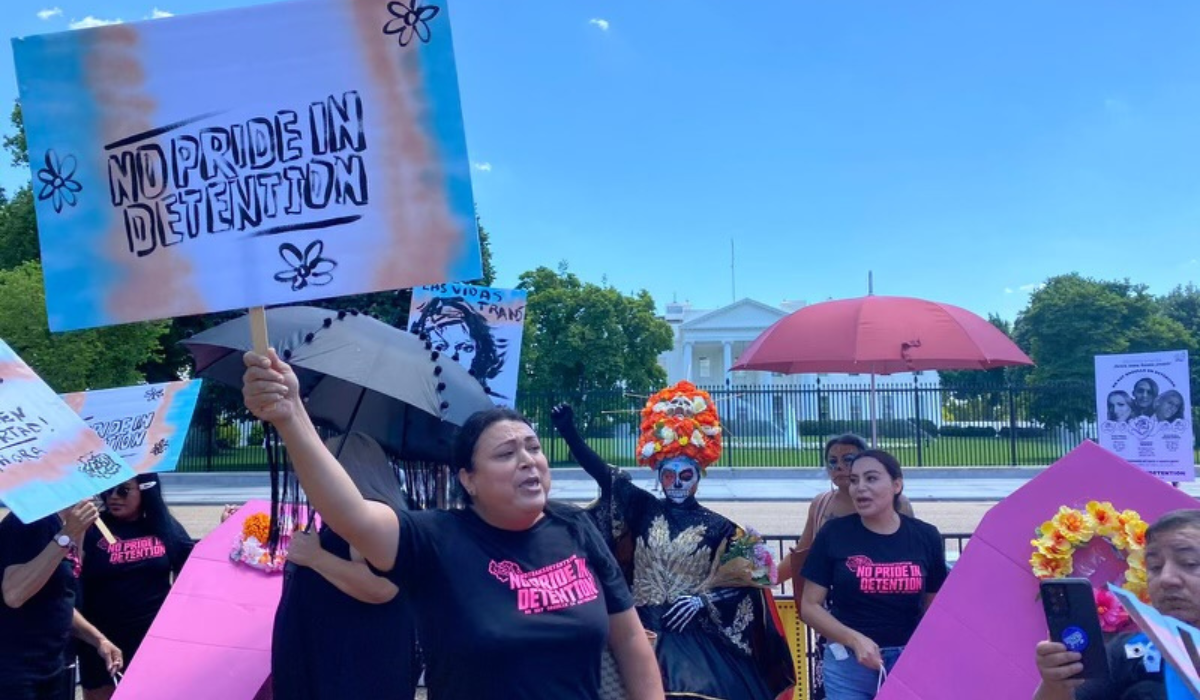 LGBTQ+ trans activists protest outside the White House holding signs in the trans flag colors reading "No Pride in Detention"