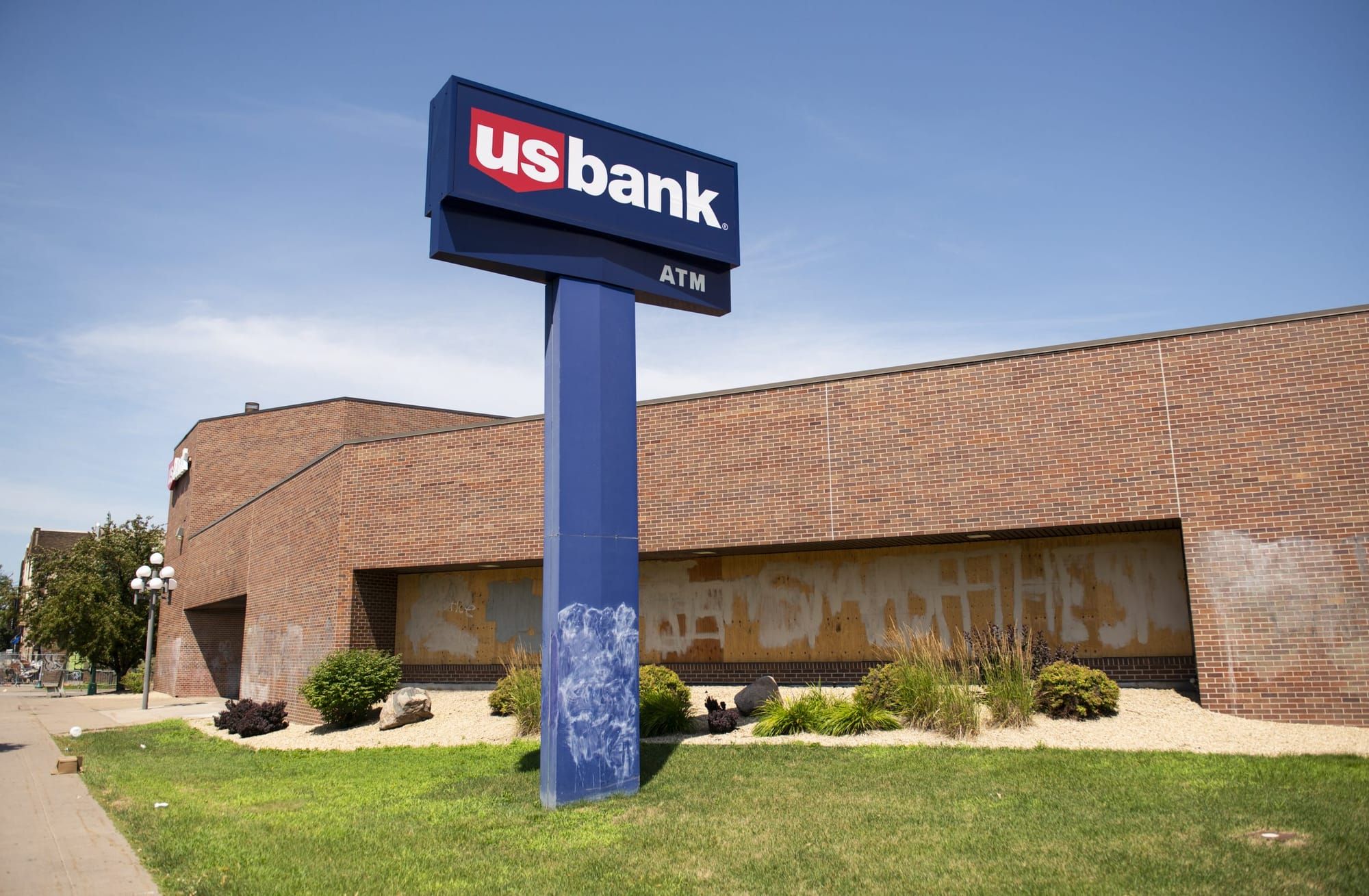 photo of a brown brick building with a patch of grass in front and a sidewalk in the foreground. a blue sign for US Bank stan