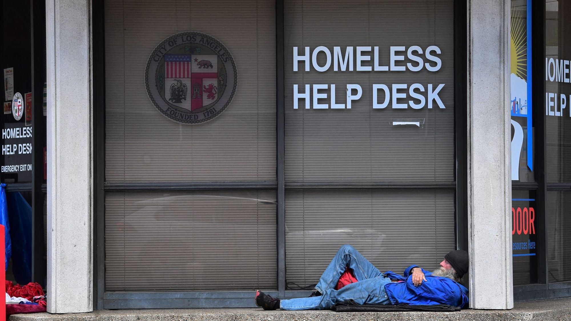 a houseless man lies on the ground outside the window for the Homeless Help Desk