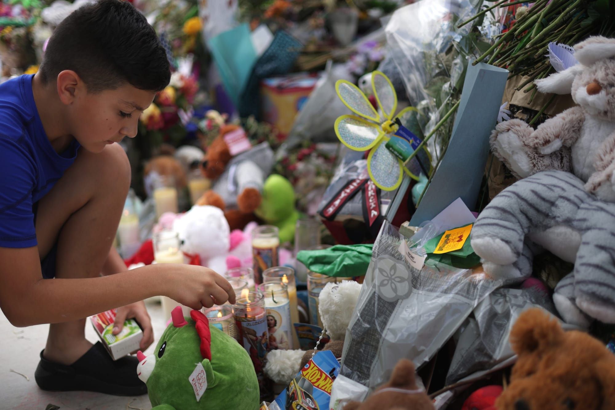 a young Latino boy kneels in front of a shrine made up of stuffed animals and flowers for victims of the Robb Elementary Scho