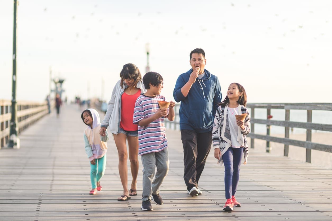 Two Filipino parents and their three children enjoy huge waffle ice cream cones on a California boardwalk by the beach. They