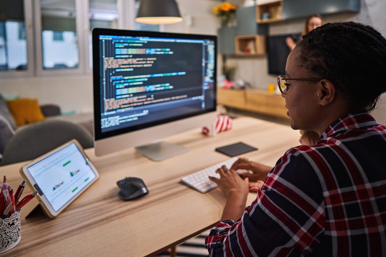 Black female computer programmer wearing a red, black, and white flannel works on a new software and coding while working fro
