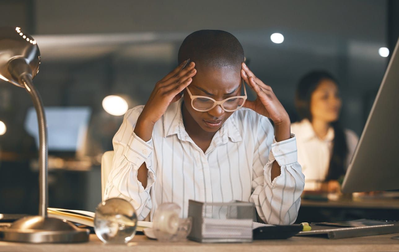 Shot of a young Black businesswoman suffering from a headache while working late in a modern office