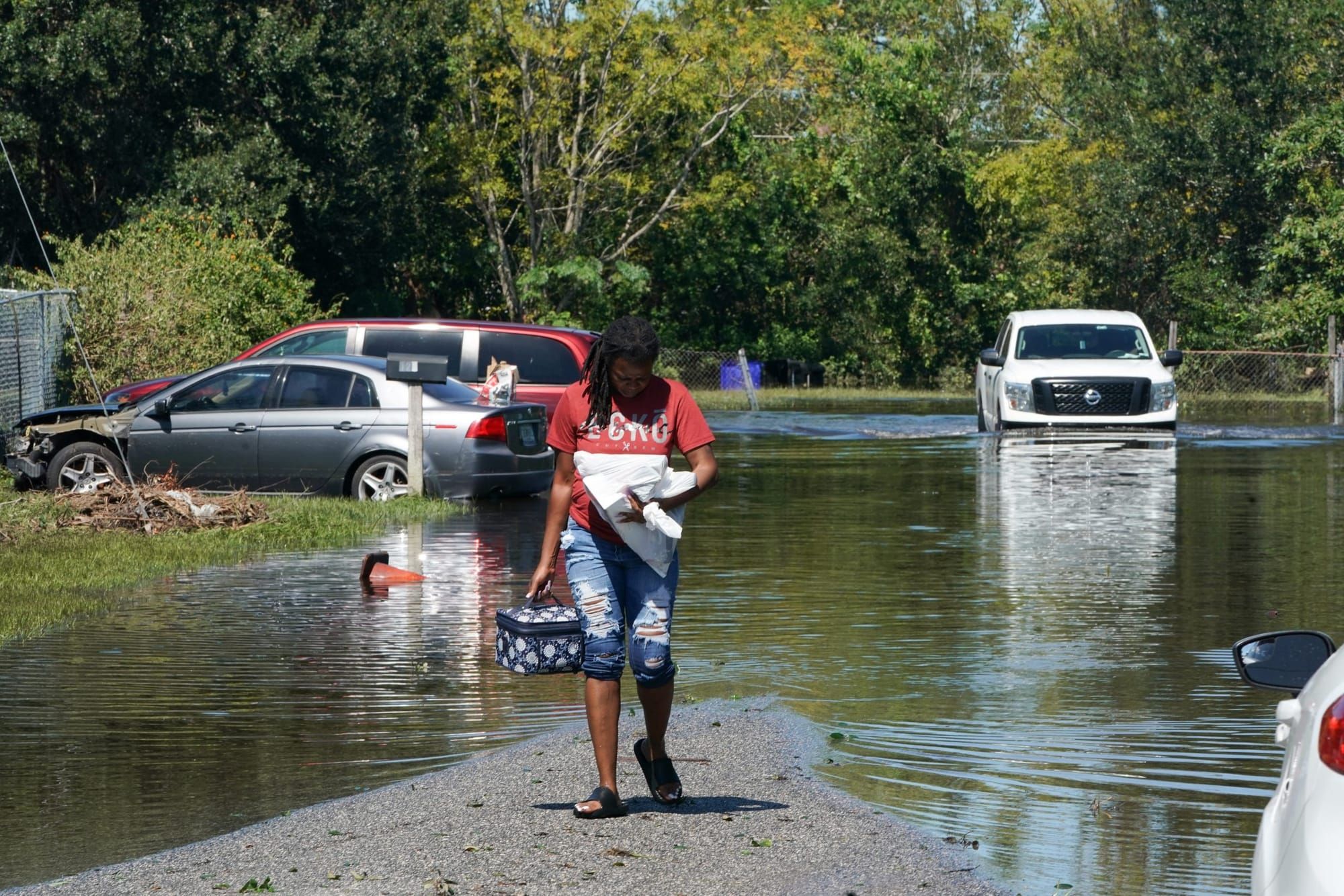 a Black woman walks in a flooded street among partially submerged cars