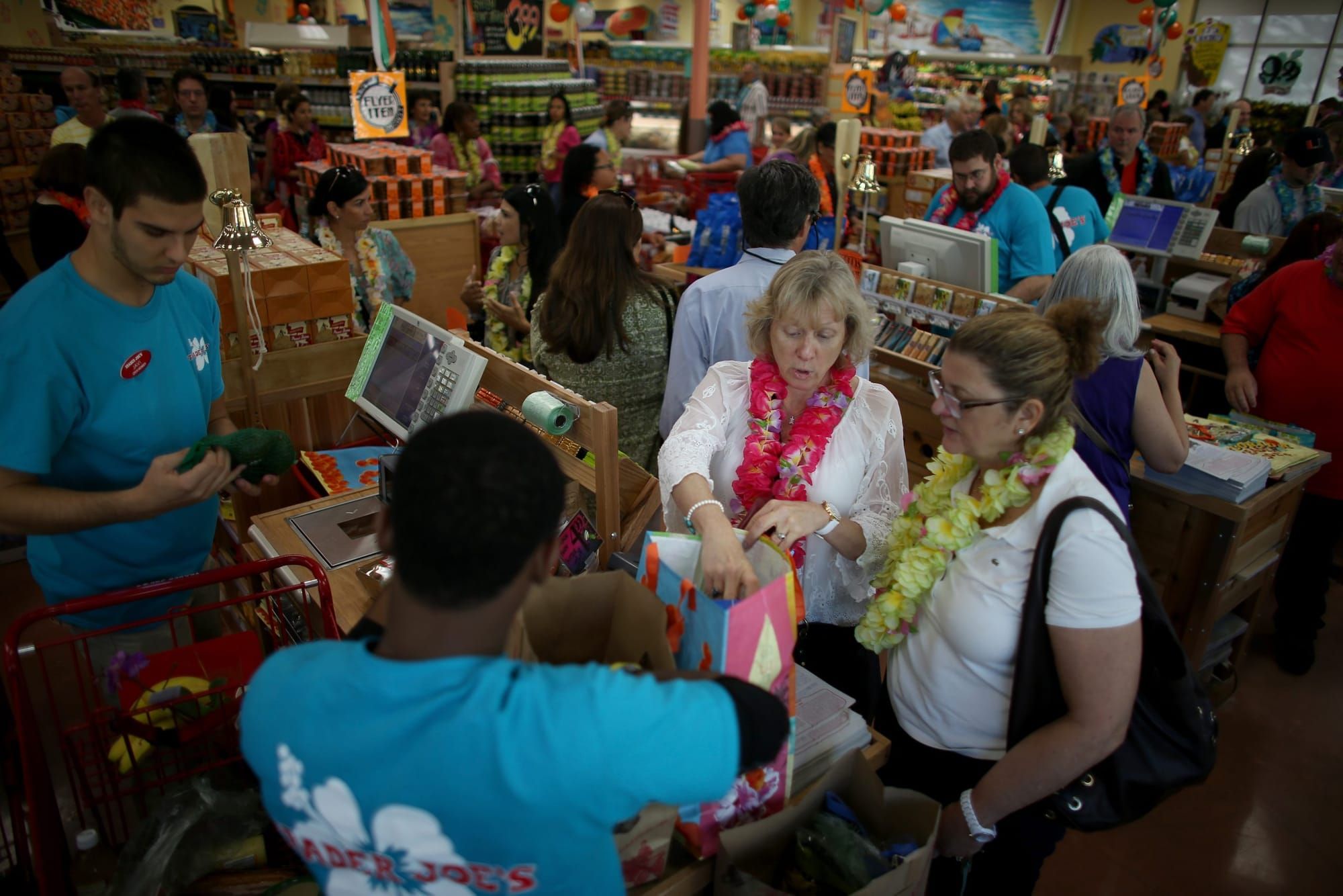 two Trader Joe's cashiers in bright blue T-shirts check out customers wearing leis