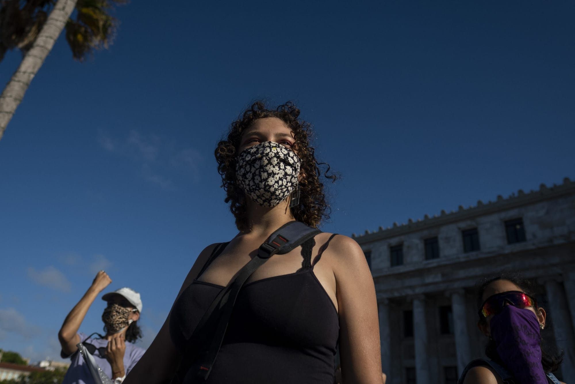 a photograph of a woman with shoulder-length curly brown hair angled from slightly below her. she stands against a clear blue