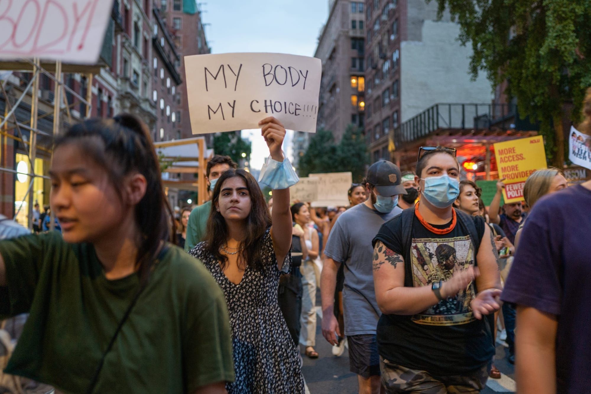 color photograph of a protest in New York City. a crowd of young women march with one woman in the mid-ground holding a white