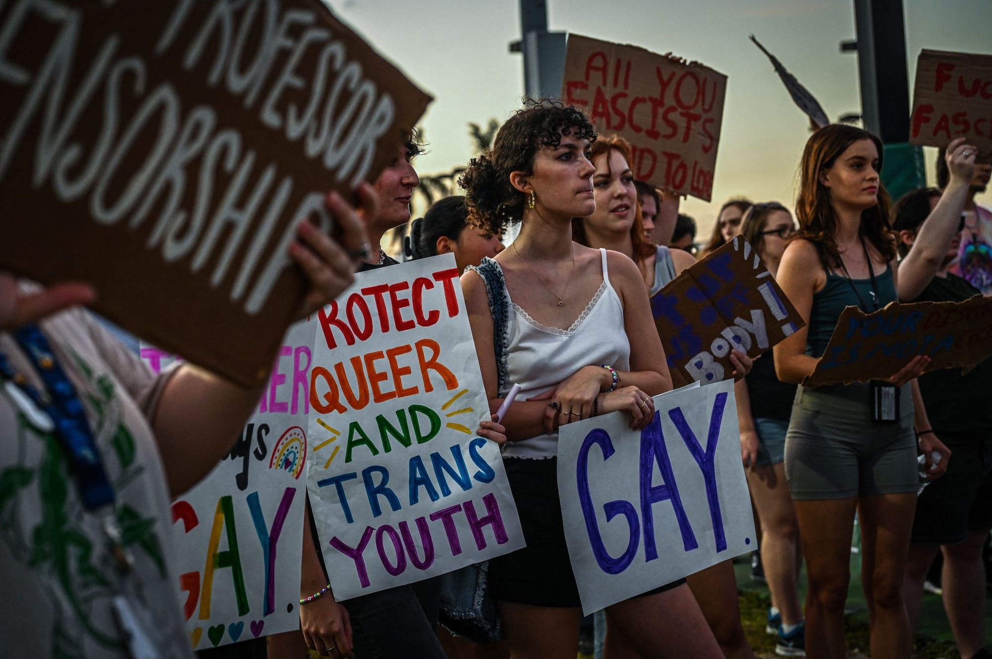 photograph of young people standing outside close together holding signs in support of LGBTQIA+ rights