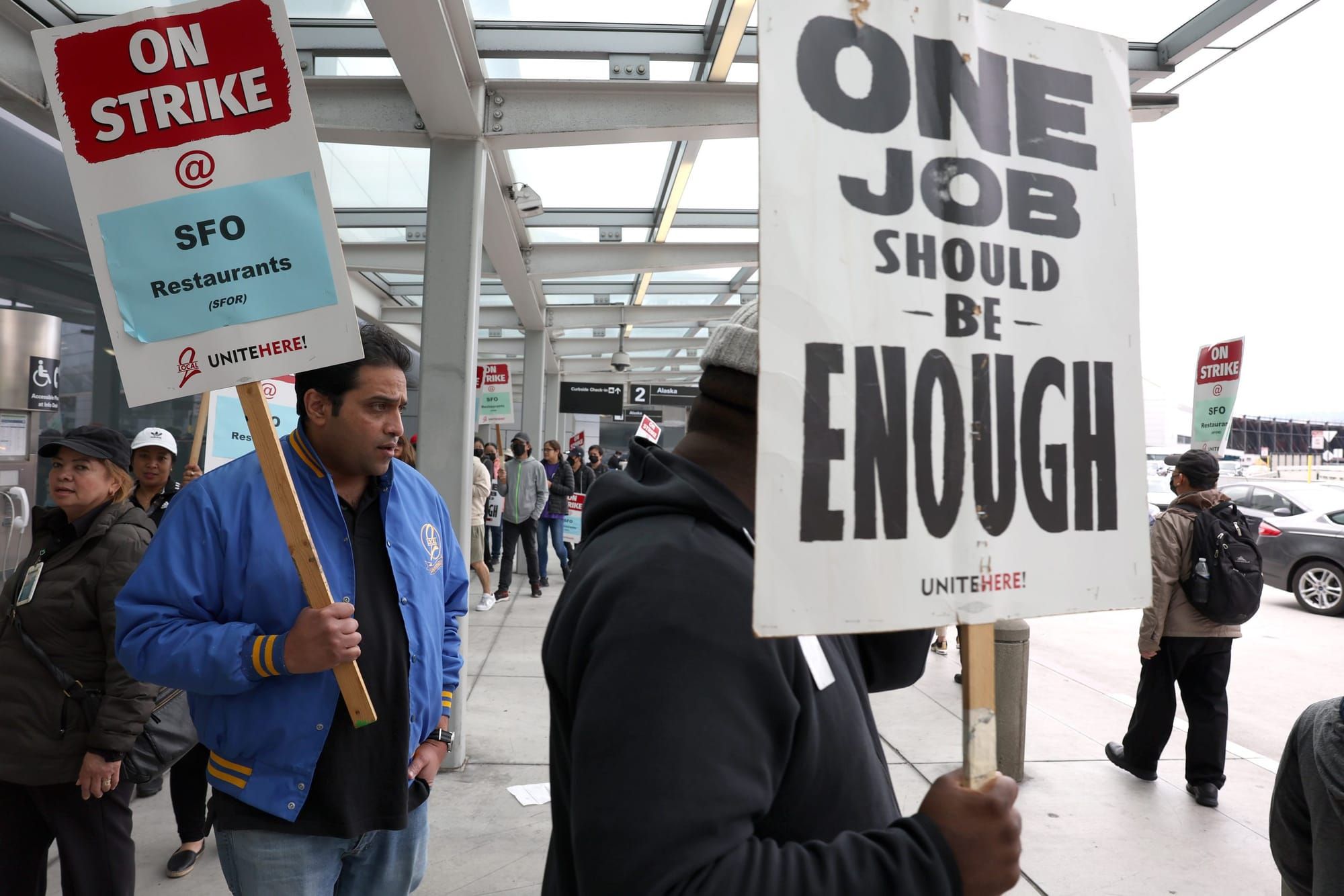 people wearing winter jackets walk in an oval around columns outside San Fransciso International Airport. In the foreground,