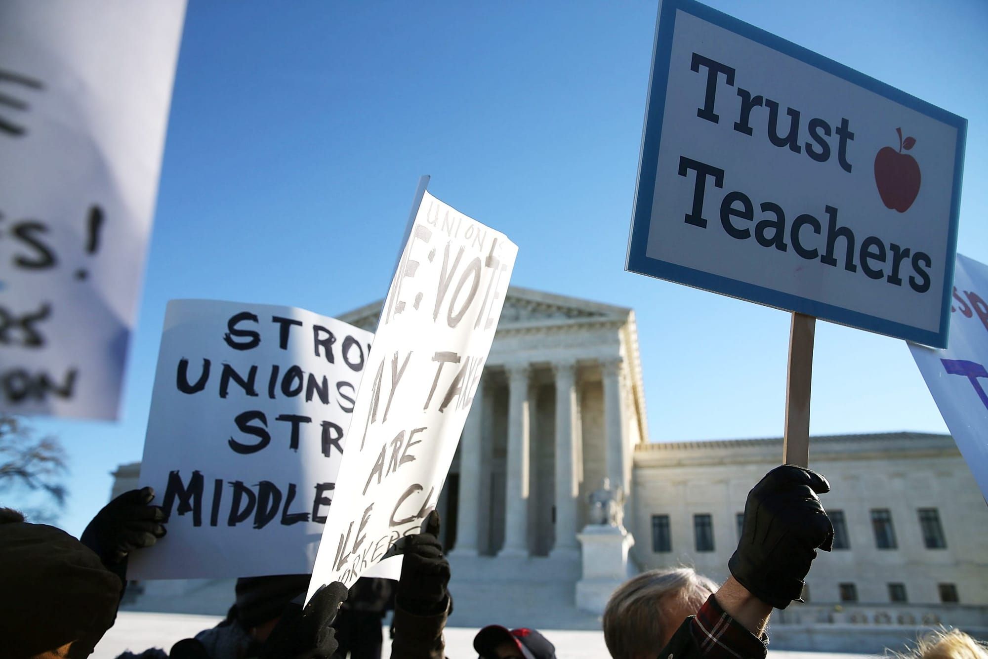 teachers stand in front of the U.S. Supreme Court building holding white paper posters with black lettering reading "Strong u