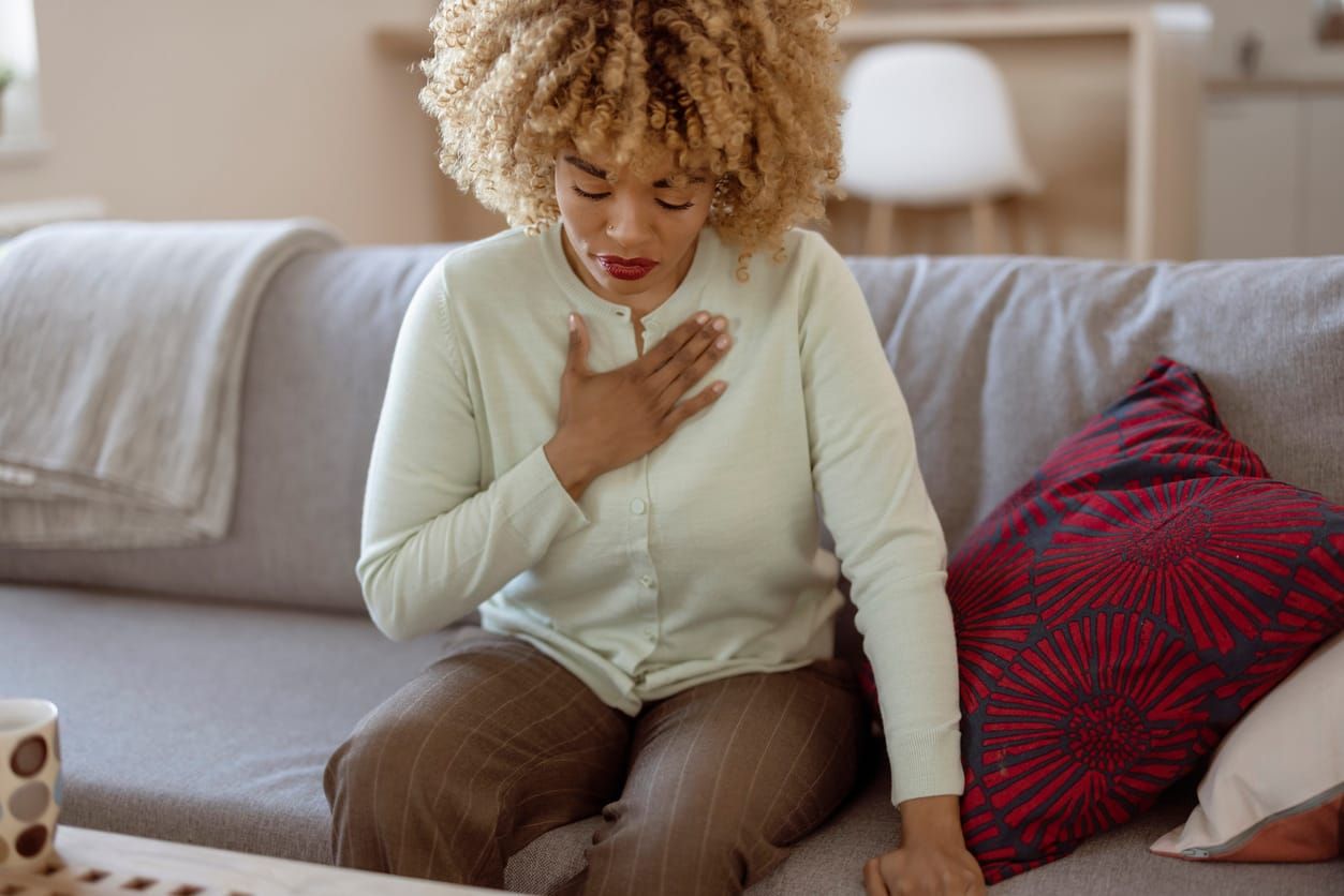 color photograph of African American woman feeling sick and holding her chest in pain while sitting on the sofa in the living