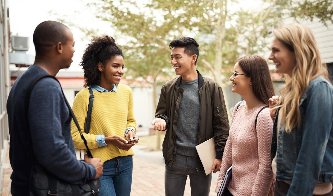 a diverse group of college students stand in a loose semicircle outside in the sunlight