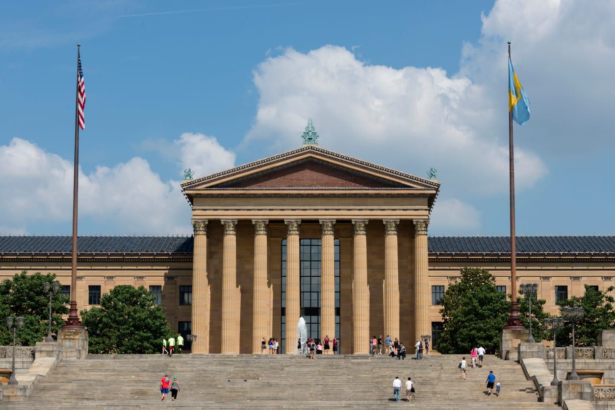 color photograph of the exterior of the Philadelphia Museum of Art. a greco-roman facade made of light brown stone sits atop