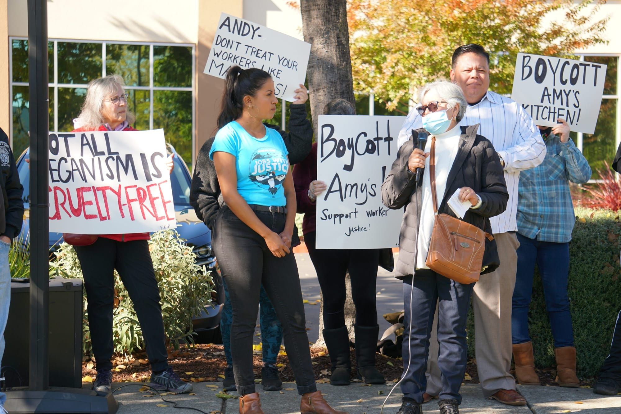 color photograph of a small crowd of about 10 people standing outside in a parking lot. they hold paper poster signs with phr