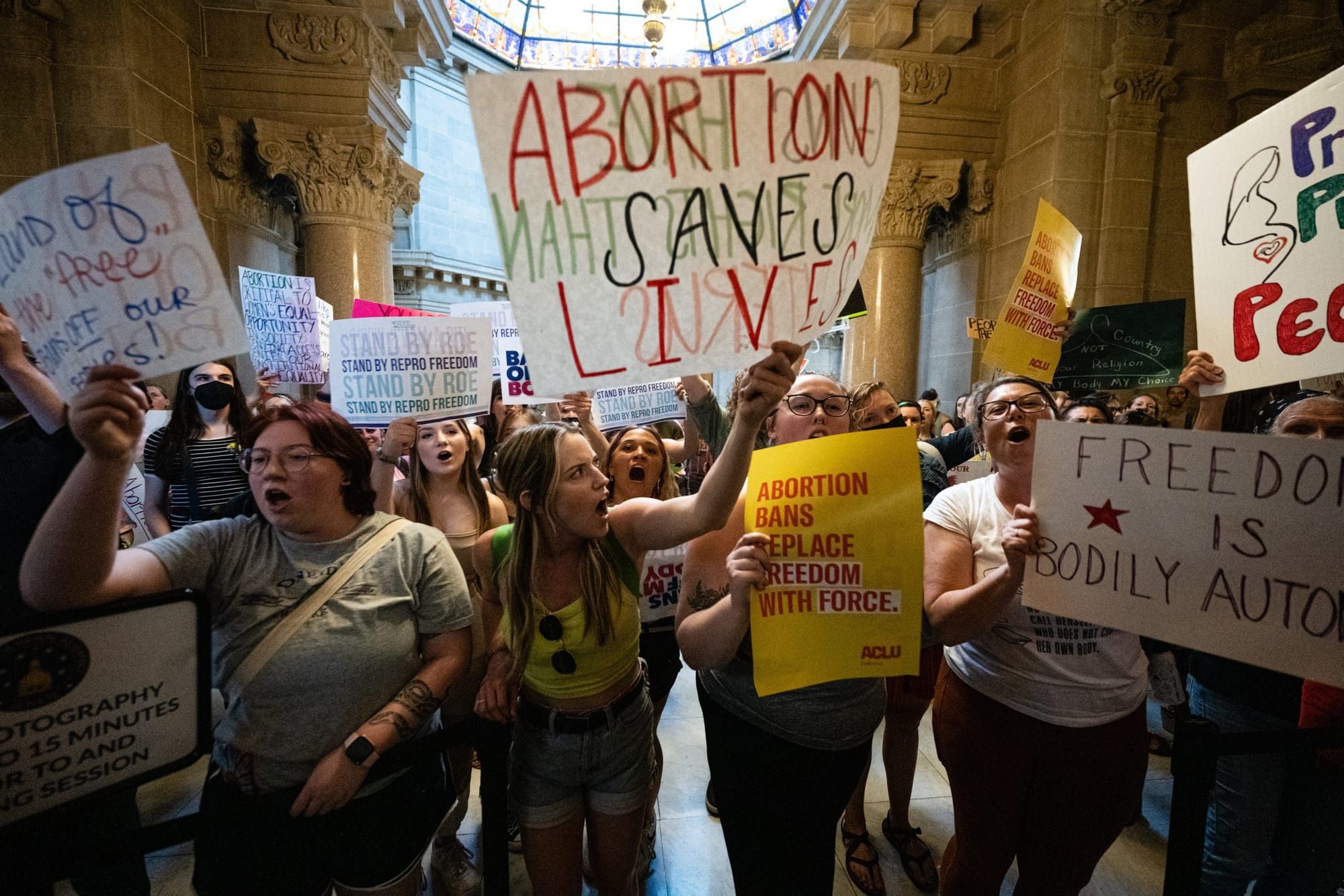 color photograph inside the Indiana State Legislature building of pro-abortion protesters holding up posters with slogans lik